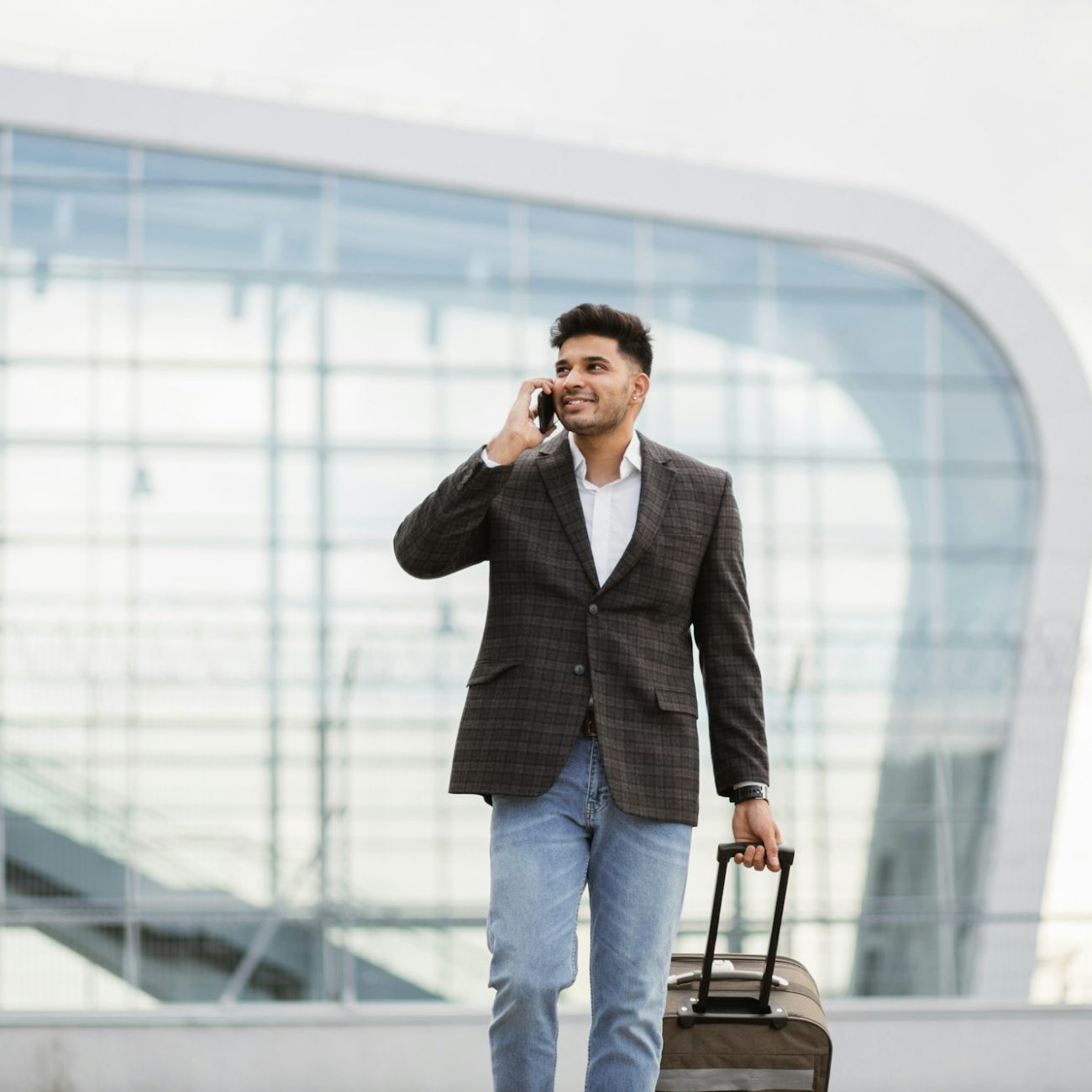 Indian business man walking outside to station or airport talking on the phone and carrying suitcase